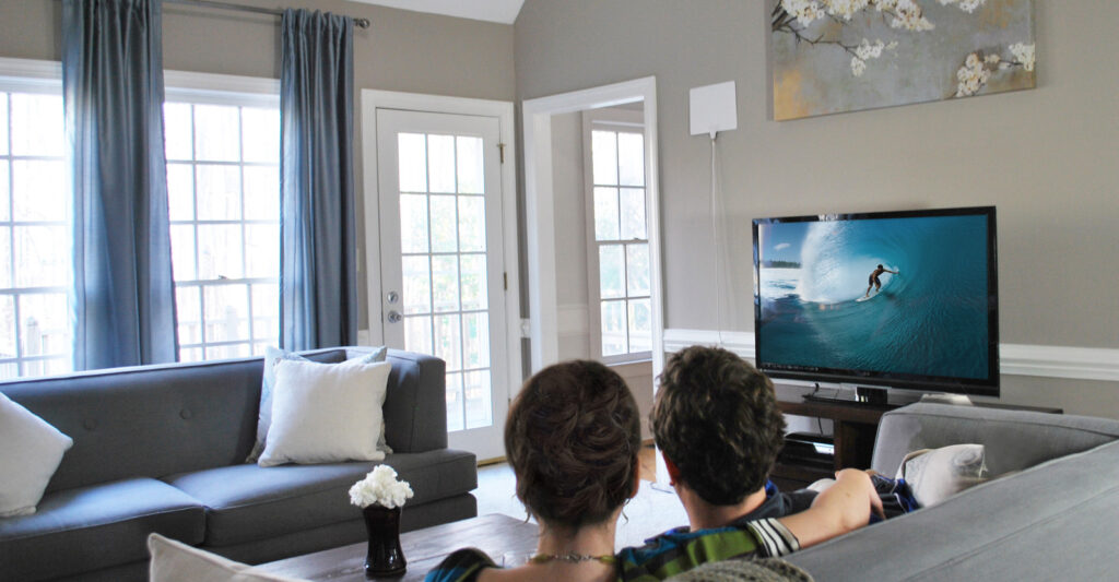 A couple sitting on the couch watching TV with a Mohu Leaf antenna hanging on the wall