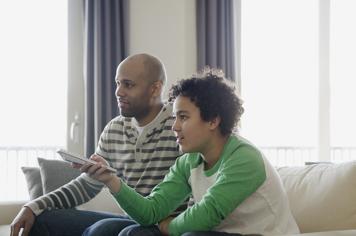 two guys watching TV one with a remote pointing at the TV